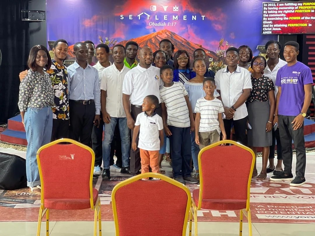 Adults and children standing together in front of a colourful stage backdrop.